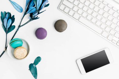 Üstten Görünüm düz renkli macarons klavye, cep telefonu ve beyaz masa mavi yapraklarda yatırın. Yaratıcı tatlı kavramı, metin alanı