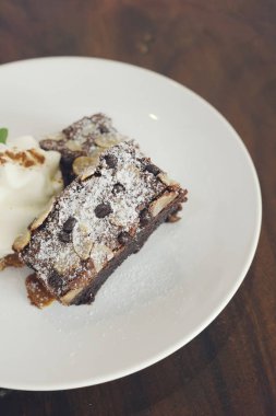 Rustik tatlı arka plan: badem, çikolatalı ve koyu ahşap masa üzerinde beyaz tabak içinde krem şanti ile kek. Metin alanı