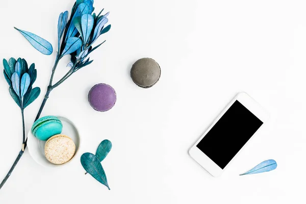Üstten Görünüm düz renkli macarons cep telefonu ve mavi yaprakları ile yatıyordu. Yaratıcı tatlı kavramı, metin alanı