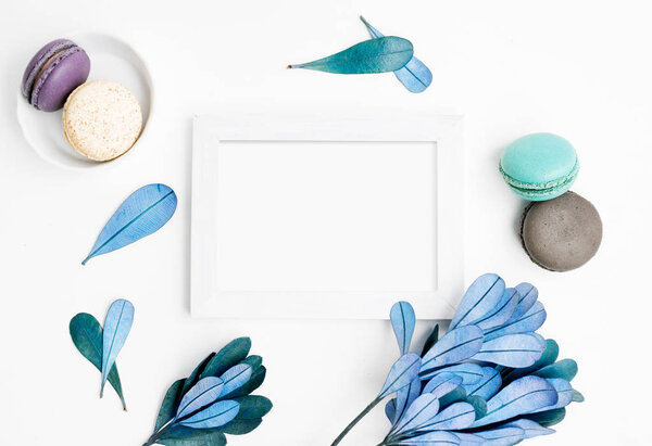 Blank photo frame mockup with macarons and blue leaves. Text space