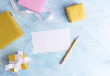 Tatil mockup: Üst azı düz altın ve pastel pembe yatıyordu hediye kutuları kalem mavi zemin üzerine beyaz kurdele, boş oyun kağıdı ile. Tebrik kartı şablonu. Yazı. Metin alanı