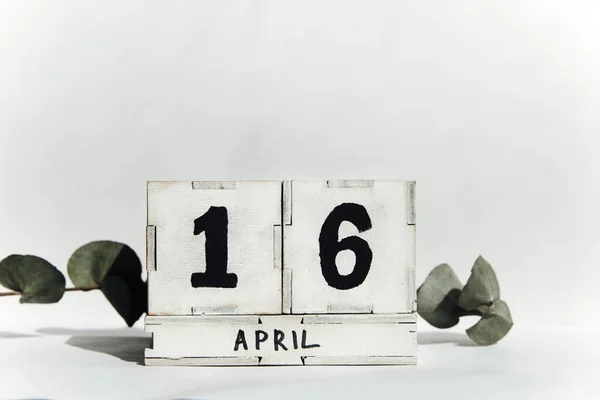 4月16日的木制立方体日历白色方块日期 绿色枝条隔离在白色桌子背景上 — 图库照片