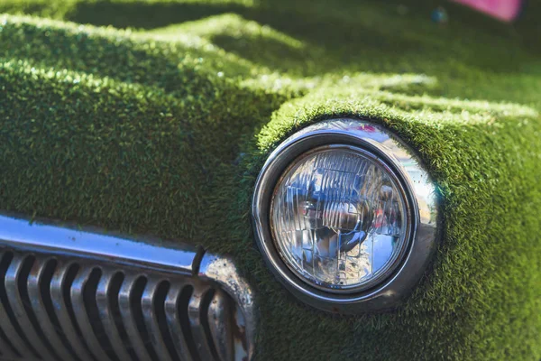 Front headlight of an old car in summer covered with artificial grass. Decorated on classical car