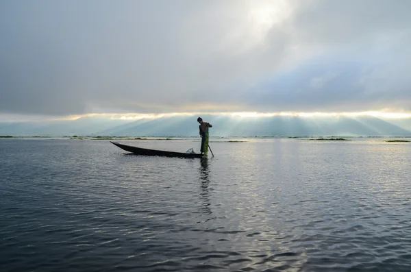 Pescador em barco de madeira lançando uma rede para a captura de peixes no lago no início da manhã antes do nascer do sol — Fotografia de Stock