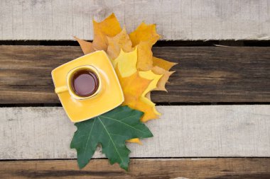 Çay bardağı ile ahşap bir masa üzerinde sonbahar yaprakları.