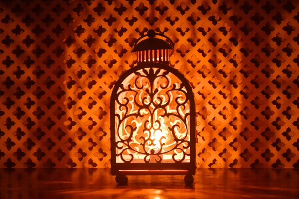 Decorative lamp with a burning candle in the night. Diffuse light from decorative perforated panels.
