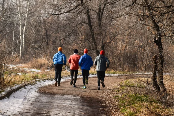 Young guys (friends) are running in the winter park. Young guys (friends) go in for sports in a winter park.