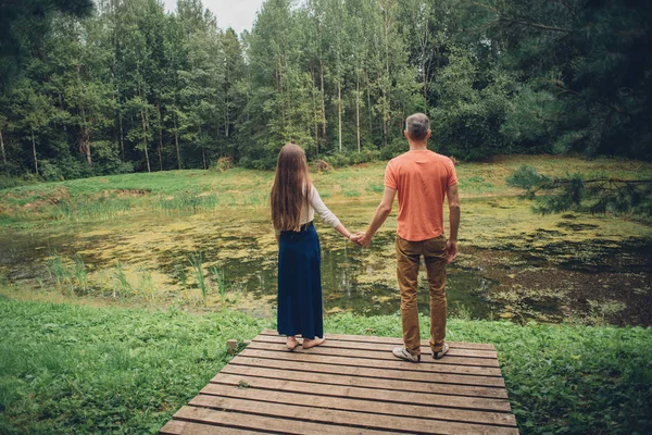 Homme et femme avec de longs cheveux un étang dans la forêt tenant la main — Photo