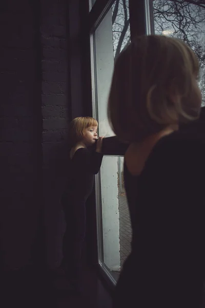 Two little girl in a black suit looks out the window — Stock Photo, Image