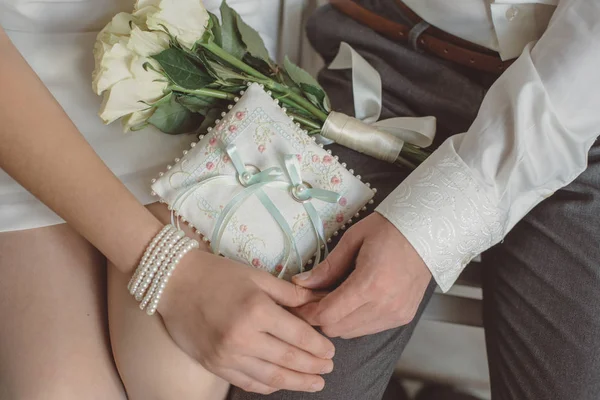 La main de la mariée dans un bracelet et marié à côté d'un bouquet de roses et oreiller de mariage — Photo