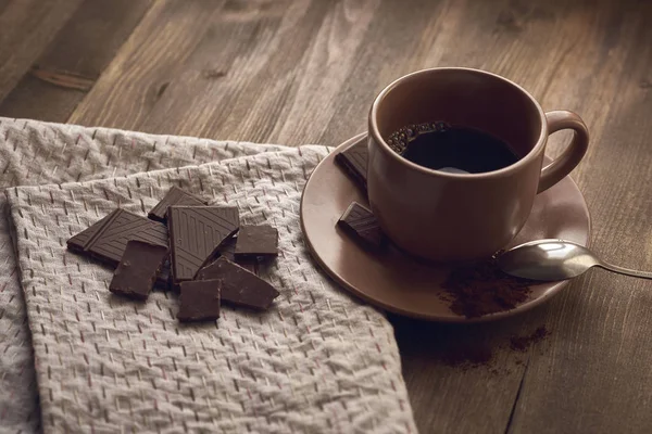 brown cup with black coffee saucer US, crushed chocolate, a spoon colored embroidered stitches gray linen towels, tablecloths on the old brown wooden background close plan