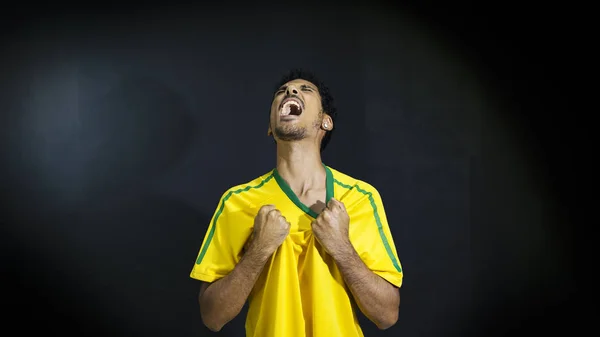 Atleta masculino o abanico en uniforme amarillo celebrando en respaldo negro — Foto de Stock