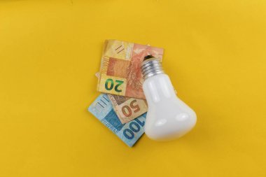 Lamp and varied values of Brazilian money isolated in yellow bac clipart