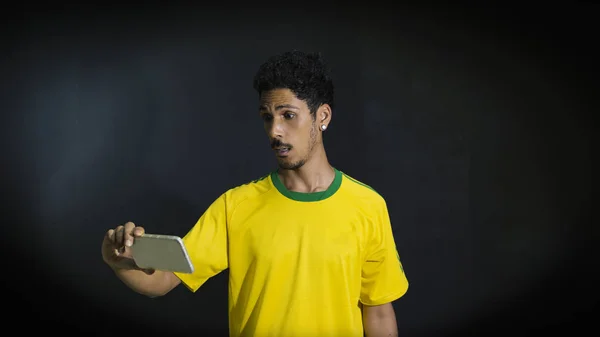 Чоловічий спортсмен або фанат у жовтій формі дивиться мобільний телефон на чорному тлі — стокове фото