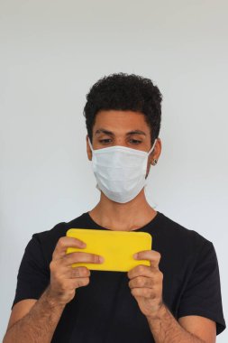 Koronavirüs maskesi takan yetişkin bir adam cep telefonunu beyaza bağlı tutuyor..