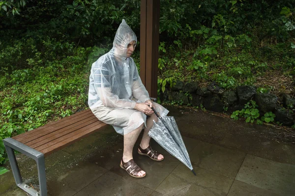 man in raincoat sitting alone on the bench