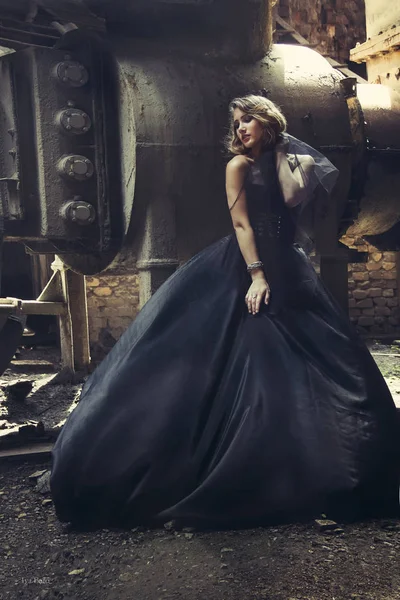 Ragazza bionda in abito nero in una vecchia fabbrica abbandonata. steampunk — Foto Stock