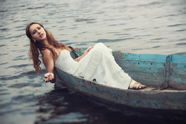 Sonhador misteriosa menina loira em um vestido branco em um velho barco no lago — Fotografia de Stock