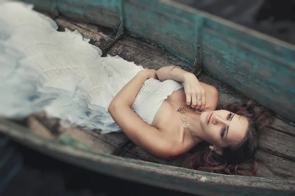 Soñadora chica rubia misteriosa en un vestido blanco en un viejo barco en el lago —  Fotos de Stock