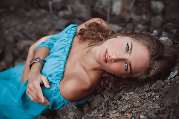 Gyönyörű álmodozó szőke lány, kék szeme egy világos türkiz ruha feküdt a kövek — Stock Fotó
