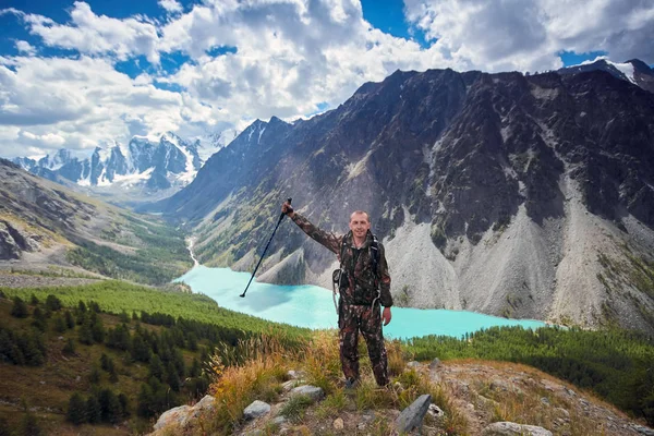 Survival in the wild. A man in camouflage resting among the mountains. Stalker, survive in the woods. Lake in the mountains. Snowy peaks, Altai