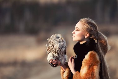 Kolunda bir baykuş ile kürk paltolu güzel bir kadın. Sarışın bir baykuş tutan doğada uzun saçlı. Bir kız romantik hassas görüntü