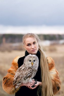 Kolunda bir baykuş ile kürk paltolu güzel bir kadın. Sarışın bir baykuş tutan doğada uzun saçlı. Bir kız romantik hassas görüntü