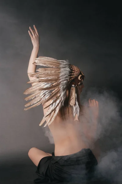 Mujer perfecta desnuda en el traje de los indios americanos en el humo sobre un fondo gris. Sombrero hecho de plumas. Misteriosa manera mística, un cuerpo sexy, una hermosa espalda —  Fotos de Stock