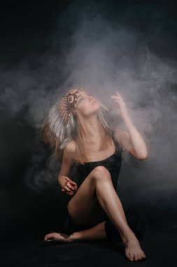 Amerika yerlileri giysi duman gri bir arka plan üzerinde mükemmel kadın. Tüyleri yapılmış bir şapka. Gizemli gizemli şekilde, seksi vücut, güzel arka. Güzel bir yüz çekici sarışın