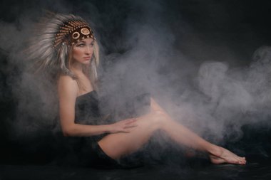 Amerika yerlileri giysi duman gri bir arka plan üzerinde mükemmel kadın. Tüyleri yapılmış bir şapka. Gizemli gizemli şekilde, seksi vücut, güzel arka. Güzel bir yüz çekici sarışın