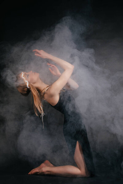 Perfect woman in garb of American Indians in smoke on a gray background. A hat made of feathers. Mysterious mystical way, sexy body, beautiful back. Attractive blonde with a beautiful face