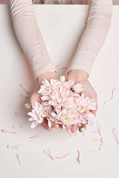 Mujer retrato de arte de moda en vestido de verano y flores en la mano con un maquillaje brillante contrastante. Chicas de fotos de belleza creativa sentadas a la mesa sobre un fondo rosa contrastante con sombras de colores . —  Fotos de Stock