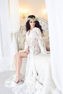 Güzel gelin iç çamaşırı ve başında, düğünden önce sabahları çiçek çelenk ile. Beyaz sabahlık gelinin düğün töreni için hazırlanıyor. Seksi kız yatakta