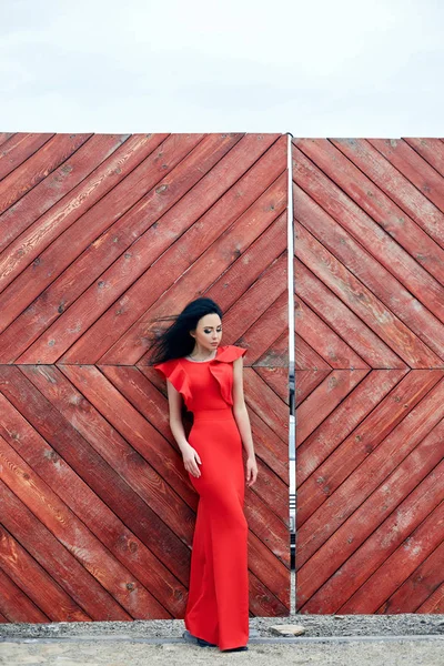 Sexy donna bruna in abito rosso è in piedi vicino al cancello rosso — Foto Stock