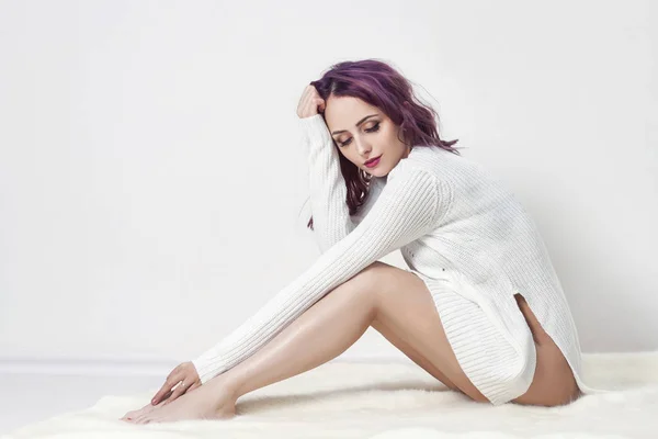 Sexig tjej med lila hår och tatueringar på sin kropp som poserar i vit skjorta på grå bakgrund. Perfekta kvinnan i vit klänning sitter på golvet, ljusa vackra makeup. — Stockfoto