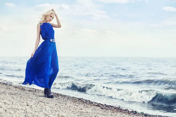 Blondin i blå klänning promenader längs strandpromenaden vid havet, sommarsemester vid havet. Vackra sensuella porträtt av en mystisk flicka. Blond kvinna i blå klänning dyker upp i vind. Sea breeze och blå vågor. — Stockfoto