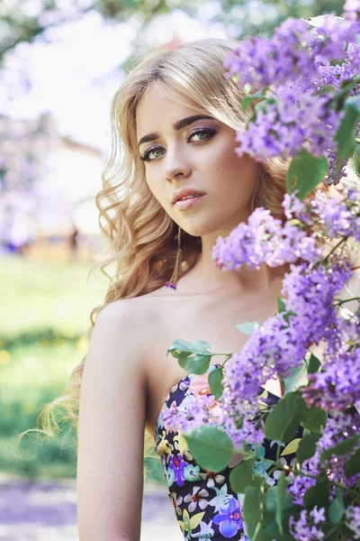 Outdoor-Mode schöne junge Frau umgeben von lila Blumen Sommer. Frühlingsblüher Fliederbusch. Porträt eines Mädchens Blondinen. — Stockfoto