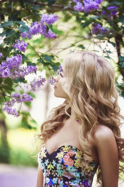 Gyönyörű fiatal nő körülvéve lila virágok nyári szabadtéri divat. Tavaszi virág lila bokor. Portré egy lány-szőke. — Stock Fotó