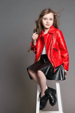 Kırmızı ceketli kız moda teşkil etmektedir ve palyaçoluk ve bir yüz yapar. Gri bir arka plan üzerinde fotoğraf stüdyosu. Doğum günü, tatil