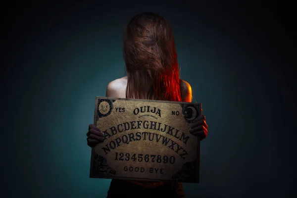 OUIJA Junta de adivinación. Chica sosteniendo una Junta OUIJA. Mujer de pelo largo y rojo Halloween. Conversación de adivinación mística con los espíritus . — Foto de Stock