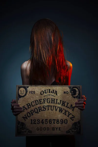 OUIJA Junta de adivinación. Chica sosteniendo una Junta OUIJA. Mujer de pelo largo y rojo Halloween. Conversación de adivinación mística con los espíritus . — Foto de Stock