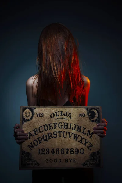 OUIJA Conseil pour la divination. Une fille tenant un conseil d'administration d'OUIJA. Femme aux longs cheveux roux Halloween. Conversation de divination mystique avec les esprits . — Photo