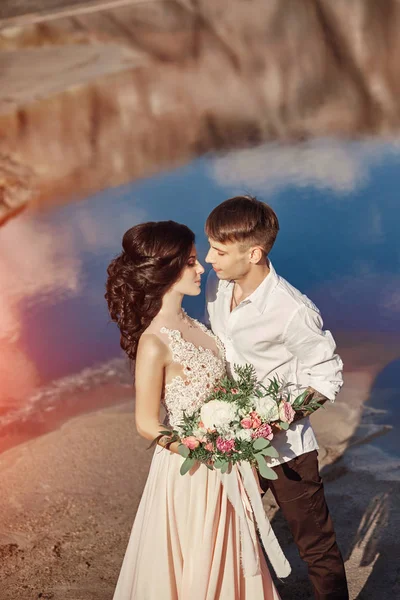 Casal apaixonado abraçando contra o fundo das montanhas e do lago vermelho. Paisagem de conto de fadas irrealista, as montanhas de Marte. Mulher com um buquê de flores nos braços dos homens . — Fotografia de Stock