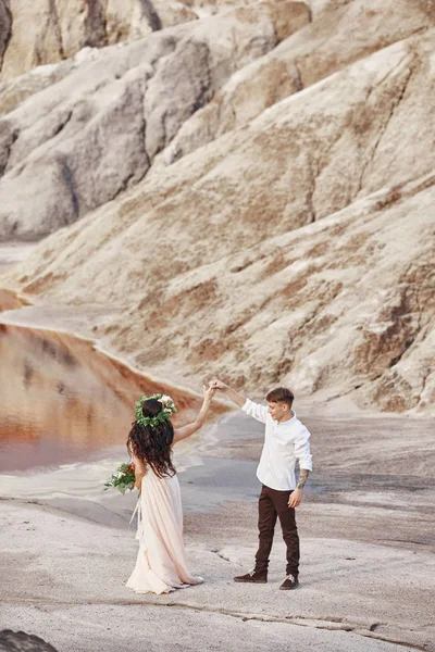 Novia y novio caminan a lo largo de las montañas rojas, escena fabulosa. Pareja enamorada cogida de la mano. Boda de otoño al aire libre . —  Fotos de Stock