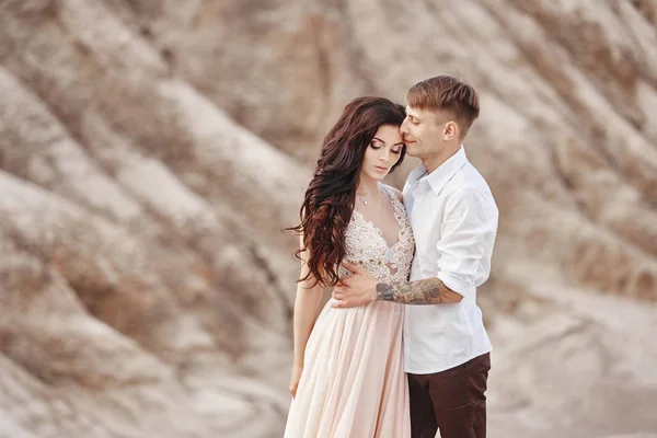 Couple se tient sur le précipice de la montagne et le lac rouge et câlins. La mariée et le marié amoureux, la femme en robe longue dans les bras des hommes . — Photo