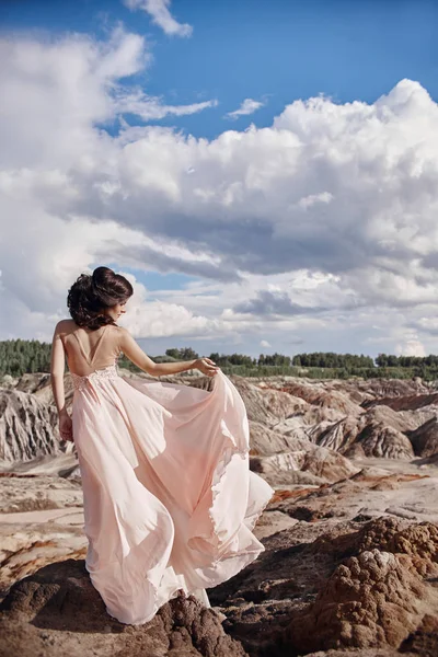 Brunett i rosa klänning står på en klippa, vinden volanger en klänning, en öm bild av en flicka. Utmärkt bergslandskap. Kvinna i vinden. — Stockfoto