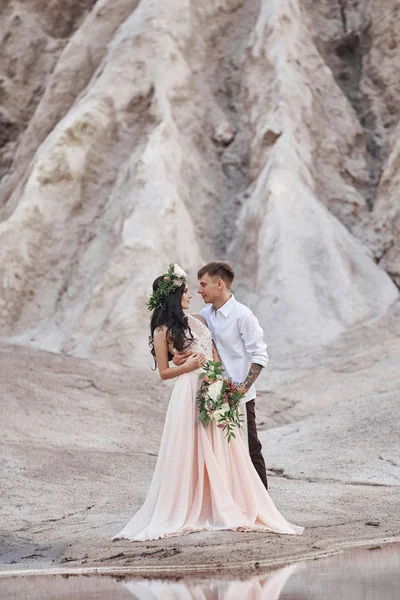 Femme avec un bouquet de fleurs dans les bras des hommes. Les mariés avec des montagnes en arrière-plan, séance photo de mariage dans la nature . — Photo