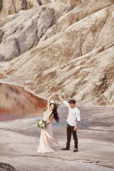 Novia y novio caminan a lo largo de las montañas rojas, escena fabulosa. Pareja enamorada cogida de la mano. Boda de otoño al aire libre . —  Fotos de Stock