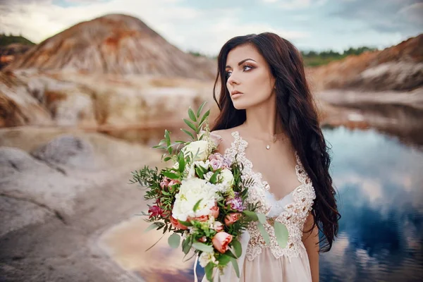 Stående kvinna med blå ögon och blombukett i händerna på naturen. Gorgeous hår och perfekt hud, vacker naturlig makeup. Flicka med en bukett rosor, mystiska dröm bild kvinna. — Stockfoto