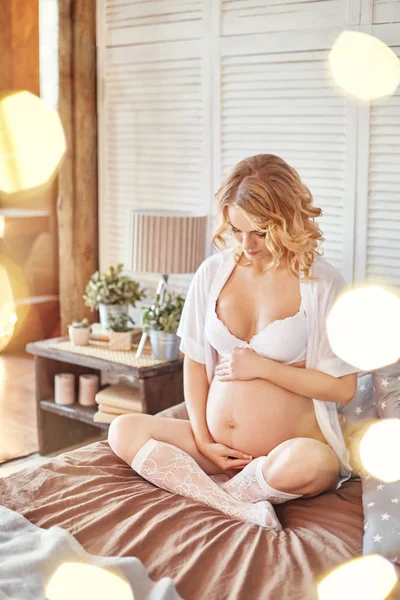 Mujer embarazada en ropa interior en mi cama. Chica rubia se prepara para convertirse en madre. El parto, la felicidad de una mujer. Mujer embarazada sexy en ropa interior blanca . — Foto de Stock